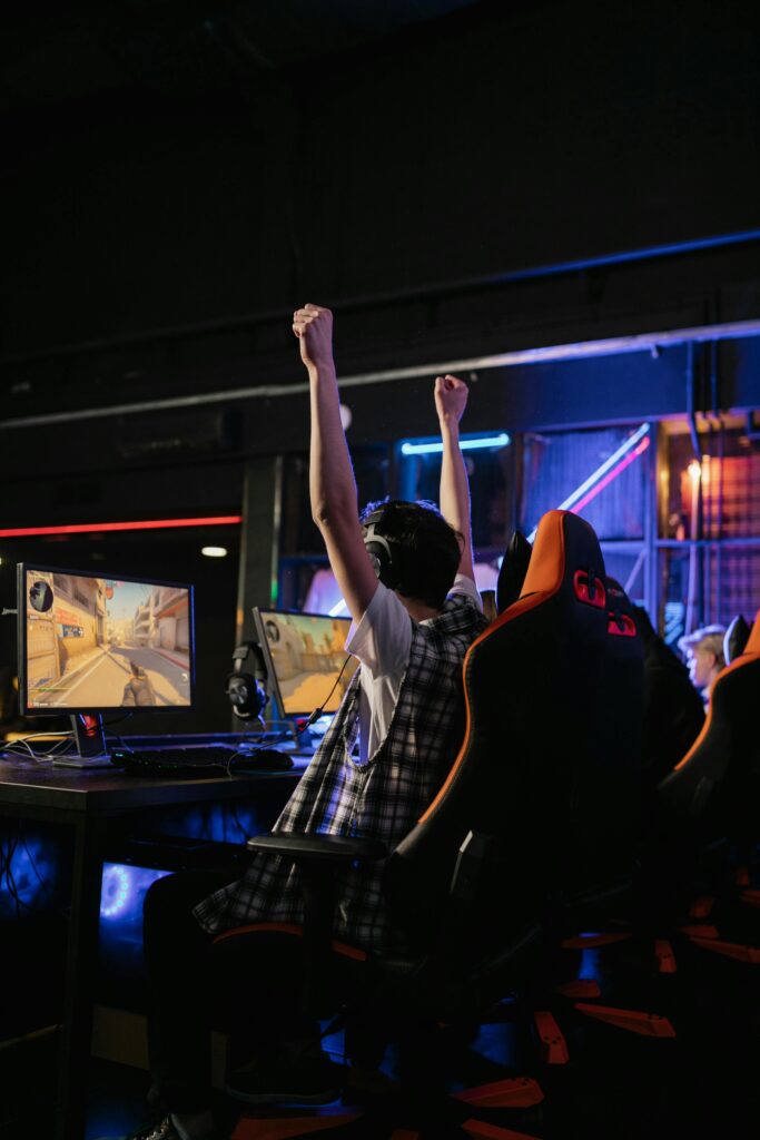 A teenage boy raises his hands in victory while playing video games in an esports arena.