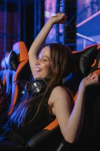 Smiling woman in gaming chair celebrating victory with arms raised, wearing headphones.
