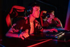 Two gamers focused on their monitors, immersed in a dimly lit gaming session.